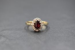 A 9ct gold garnet and white gemstone set cluster ring, the central oval cut garnet in a ten white