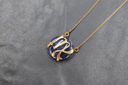 A sodalite pendant, the polished disc mounted in a yellow metal 'M' setting, on an mounted 18ct gold