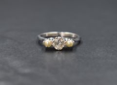 An 18ct white gold pearl and diamond set trilogy ring, the central old cut diamond measuring