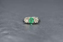 An early 20th century white metal emerald and diamond three stone ring, having a central baguette