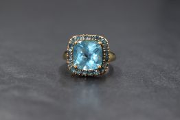A 9ct gold blue topaz ring by QVC, the central cushion cut blue topaz within a halo surround of