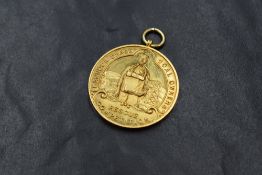 A 1930's 9ct gold medalion of circular form with loop, having moulded mining scene and inscribed '