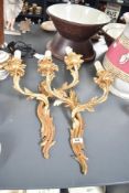 A pair of cast-gilt metal two-branch wall lights, of sinuous foliate from with simulated candle