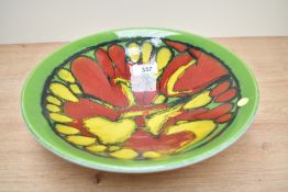 A Poole pottery bowl decorated with red and yellow designs on a green ground, painted 'AA' and '