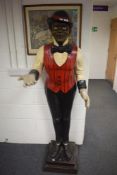 A life-size moulded plastic butler statue wearing red and black stripe waistcoat, stood on a two st