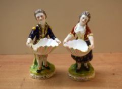 A pair of continental hand-painted porcelain figures both carrying clam shells, both with markings
