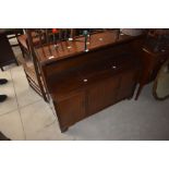 A mid-century mahogany style sideboard having book shelf below three cabinet doors decorated with
