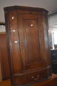 A George III oak corner cupboard, with dentil moulded frieze, panelled door and base drawer, between