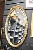 A reproduction oval mirror having ribbon style decoration and bevelled edge, h61cm
