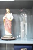 A moulded and painted plaster figure of Jesus, housed under a blown glass dome with circular stand