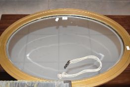 An oval gilt-painted and bevelled mirror, of 1920's design with reed and bead moulding 86cm x 61cm