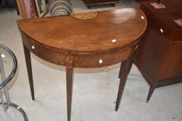 A 19th Century mahogany demi lune fold over table having inlaid acorn decoration in the Sheraton