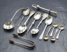 A collection of silver and white metal flatware, including a white metal mechanical pickle grab with