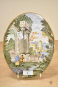 A maiolica style oval plaque depicting a landscape with architectural ruins and figures in the