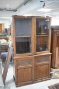 An early/mid 20th century oak bookcase over cupboard, having a foliate lunette moulded cornice