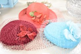 Three ladies fascinators or wedding hat / headpieces, each with a net veil, in red, burgundy and