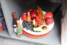 A decorative display of wooden, stone and synthetic fruit, within a white ceramic bowl with red