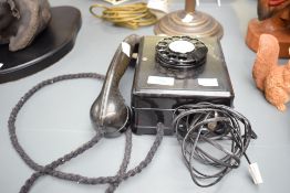 A vintage black wall-mounted rotary dial telephone.