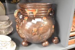 A brown glazed pottery vase decorated with geometrical patterns, two handles and raised on ball