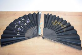 Two Victorian handheld fans in black silk, one having gold and brown floral hand-embroidery, the