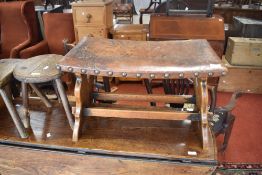 A traditional oak stool having studded leather bowed top, width approx. 63cm
