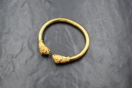 An 18ct gold lion head hinged bangle, the two lion heads having ruby set eyes on a textured bangle