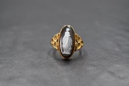 A yellow metal presumed gold agate cameo set ring, the oval cameo depicting a standing maiden in