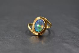 An 18ct gold oval black opal ring, the cabochon stone being in a closed collared mount to cross over