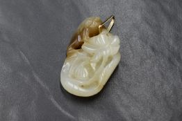 A Chinese carved white and rust jade style pendant depicting a fish with a lily flower having a