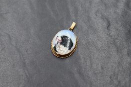A painted ceramic oval panel depicting a King Charles Spaniel in a 9ct gold pendant mount with twist
