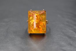 A yellow metal Baltic amber ring having a large tubular shaped stone in a six claw wired mount on