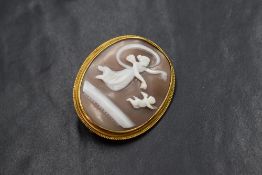 An oval conch shell cameo brooch depicting Aurora the goddess of dawn accompanied by the Genius of