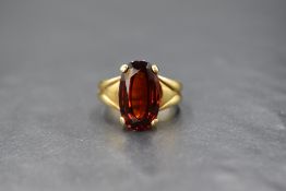 A yellow metal garnet ring stamped 18ct, the large oval garnet being in a four claw raised mount