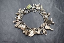 A white metal charm bracelet, presumed silver having 26 charms, many stamped silver/900 plus three