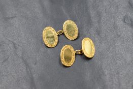 A pair of 9ct gold cufflinks having plain oval panels with engraved borders and chain connectors,