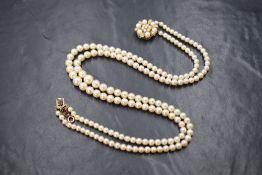 A double string of cultured pearls of graduated even form having a large 9ct gold floral pearl set