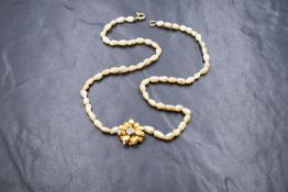 A string of baroque seed pearls with central diamond set yellow metal flower pendant, no marks but