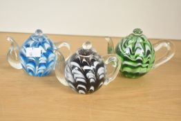 A selection of three studio glass ornamental teapot paperweights, featuring a swirled pattern of