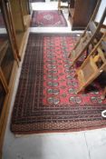 A Persian rug, in the Bokhara style having red ground with cream and russet detailing, areas of wear