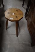A traditional golden oak milking stool having octagonal top on chamfered splay legs