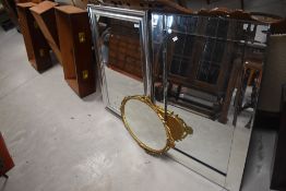 A group of three mirrors, comprising a small oval ornate cast gilt metal mirror, a modern silvered