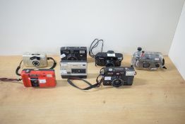 A group of several 35mm cameras and a disc camera. Canon Sure Shot 80 Tele, a Snap Sights 35mm
