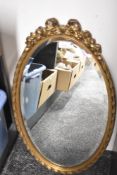 A reproduction oval mirror having ribbon style decoration and bevelled edge, h61cm