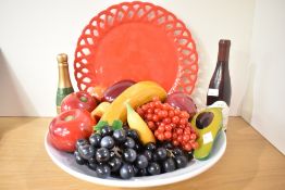 A decorative display of wooden, stone and synthetic fruit, within a white ceramic bowl with red