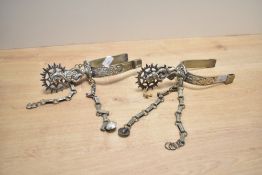 A pair of 20th-century white metal spurs, with a revolving spiked wheel, of ornate decorative