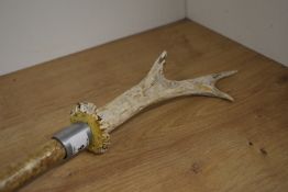 A wooden walking stick with a metal feral at each end and an antler mounted on the top to form a