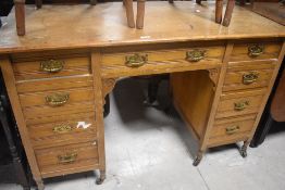 A late Victorian light oak kneehole desk, of traditional arrangement with brass back plates and bale