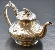 A William IV silver teapot, having an acorn finial over a squat bulbous body with floral scroll
