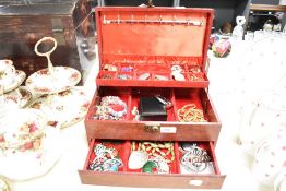 A red faux leather jewellery box containing an assortment of costume jewellery, including a teddy