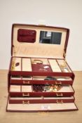 A red leather jewellery box having multiple shelves, ring holders and compartments, containing a
